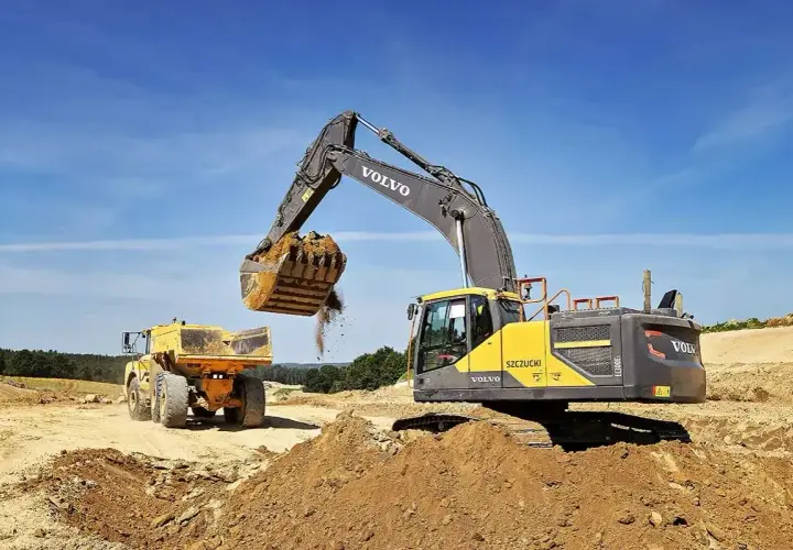 Koparka Volvo zasypuje wykop, przygotowując teren pod ułożenie rur. Cennik usług bez materiału.