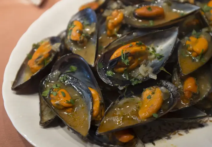 Un plato lleno de mejillones a la marinera, jugosos y con perejil picado, listos para disfrutar.
