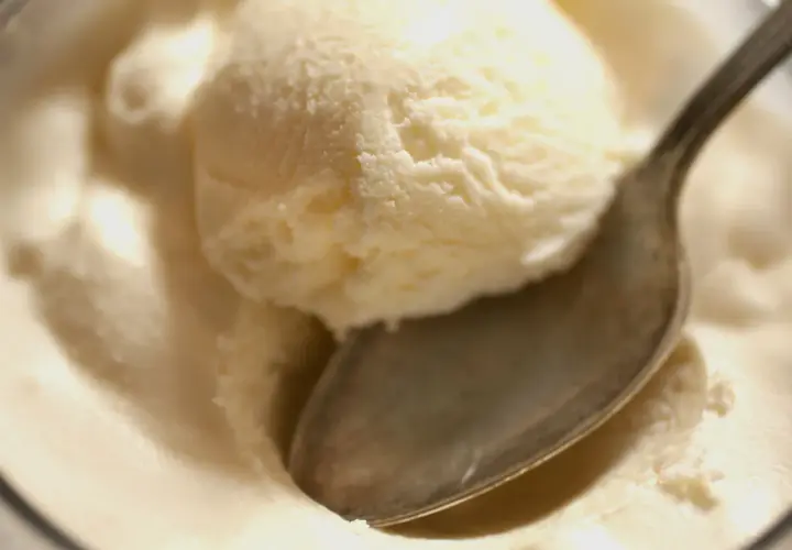 Kremowe lody z serka wiejskiego, idealne na deser. Łyżeczka zanurzona w słodkiej masie.