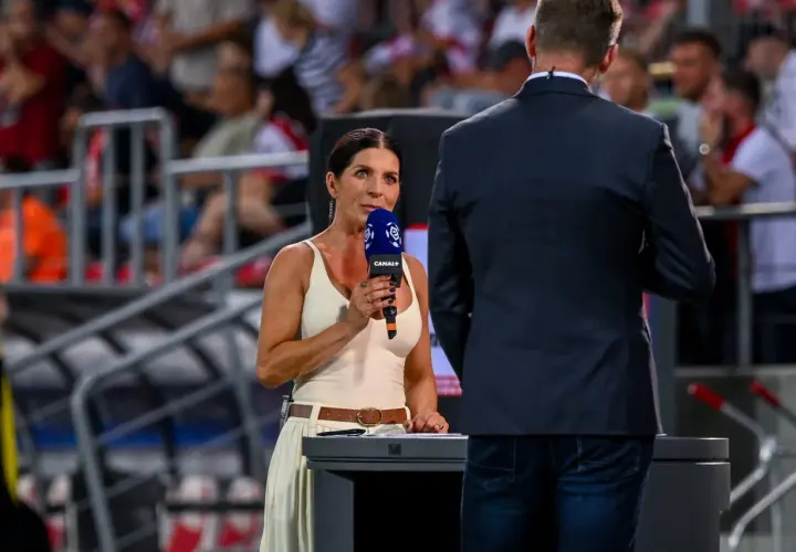 Kobieta z mikrofonem Canal+ na tle trybun stadionu.