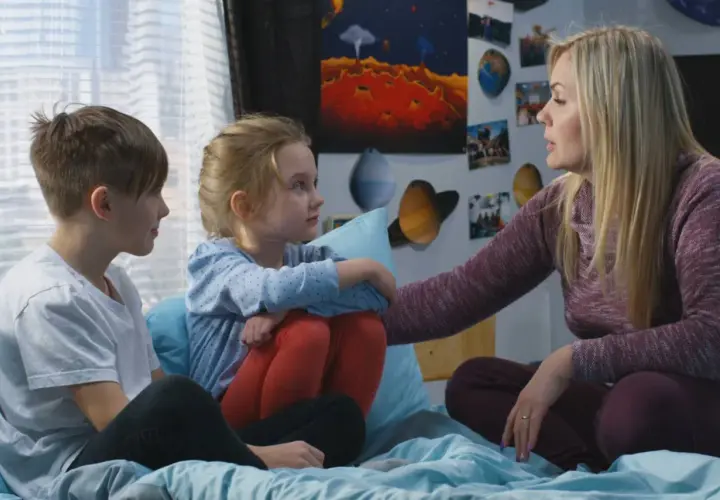 Kobieta z dwójką dzieci, otoczona plakatami kosmicznymi, rozmawia o przyczyny popularności motywu "found family" w literaturze przygodowej.