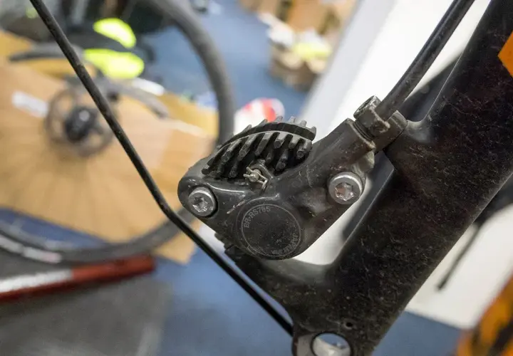 Close-up of a bicycle's hydraulic disc brake caliper, showing the brake fluid top and cooling fins.