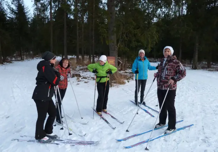 Grupa osób w strojach na narty biegowe przygotowuje się do jazdy w lesie.