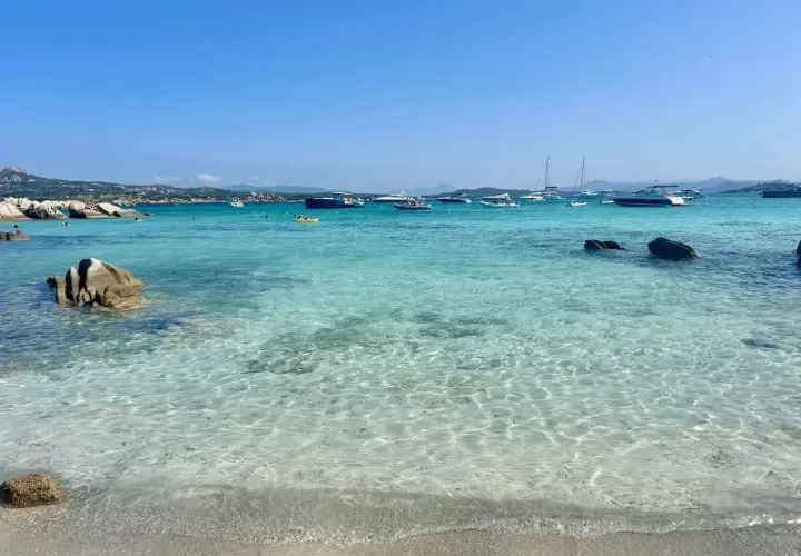 Plage de rêve en Sardaigne, eaux turquoise cristallines, rochers, bateaux au mouillage. Un coin de paradis pour savourer la ciaccia sarde.