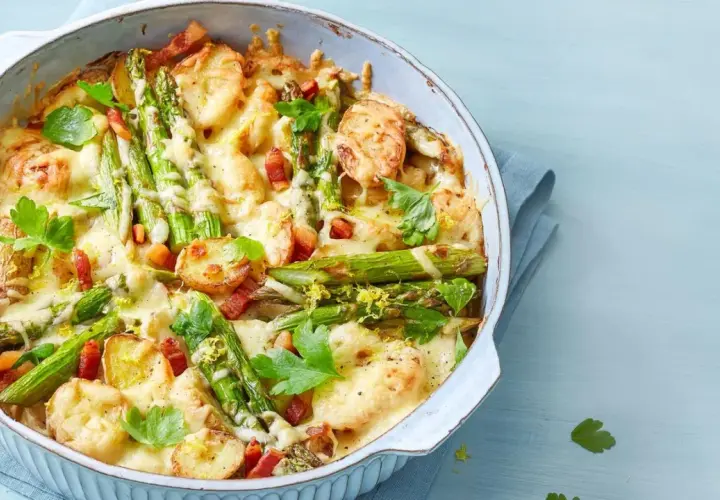Herzhafter Spargel Auflauf mit Kartoffeln, Speck und geschmolzenem Käse, garniert mit Petersilie und Zitronenschale.