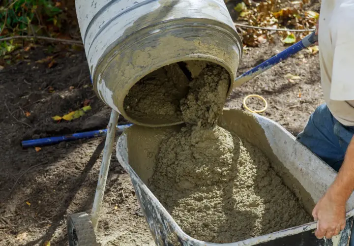 Mieszanka betonu z betoniarki trafia do taczki. Trudno ocenić, ile piasku na worek cementu, ale efekt widać.
