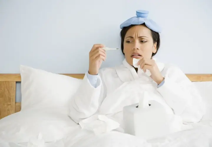 Donna a letto con impacchi freddi in testa, termometro e fazzoletti, preoccupata per la sua salute, quasi un'ipocondriaca.