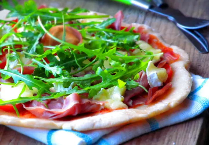 Pyszna pizza parma z rukolą i serem pleśniowym, gotowa do pokrojenia.