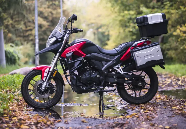 Czerwono-czarny motocykl szosowo turystyczny 125 z kuframi, gotowy na jesienne wyprawy po leśnej drodze.