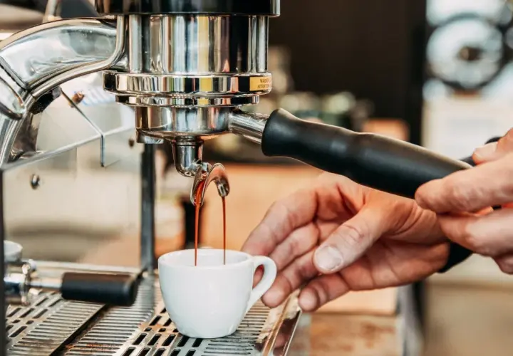 Frisch gebrühter Espresso fließt aus der Maschine in eine kleine Tasse. Die Zubereitung von handgebrühtem Kaffee ist ein Kunstwerk.