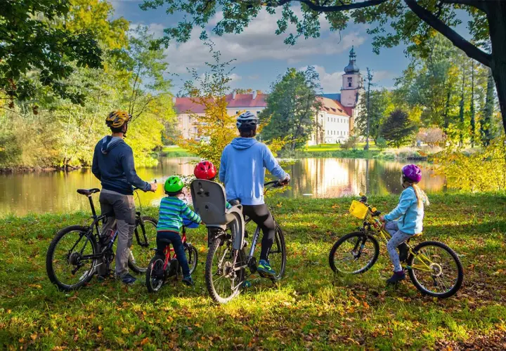 Rodzina na rowerach podziwia jesienny krajobraz krainy Górnej Odry. W tle pałac i jezioro.