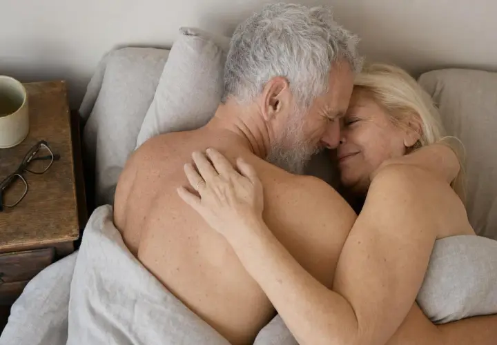 Coppia anziana abbracciata nel letto, un'immagine che dimostra come fare l'amore fa bene, portando serenità e intimità.