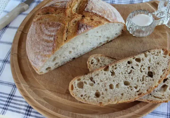 Pyszny chleb pszenno żytni na zakwasie, pokrojony na desce, z solniczką i nożem w tle. Idealny na śniadanie.