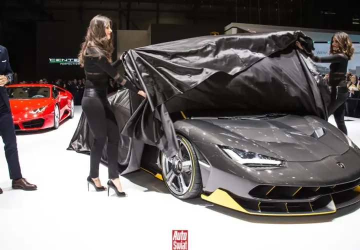 Elegancki mężczyzna i dwie kobiety odsłaniają nowy, szary Lamborghini Centenario. Obok stoi czerwony sportowy samochód.