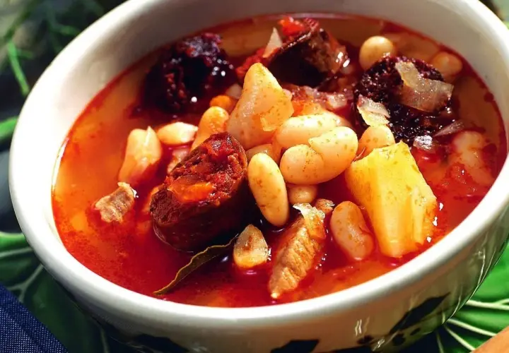 Un reconfortante plato de alubias con chorizo, trozos de patata y carne en un caldo rojizo.