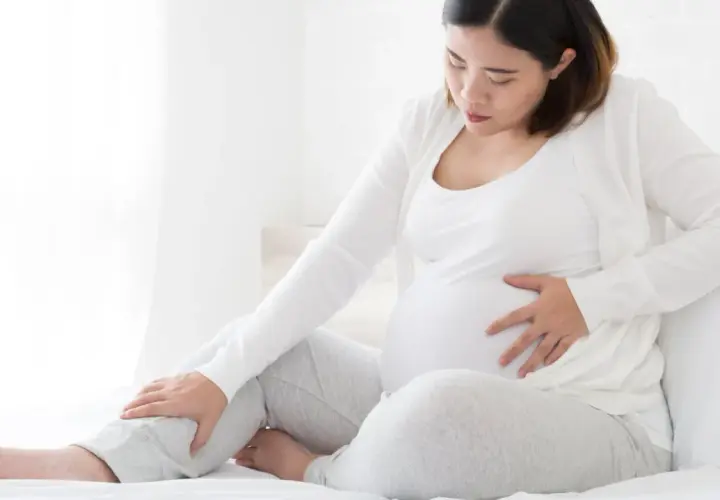 Schwangere Frau mit Hand auf dem Bauch und Bein, die Beschwerden oder Kompression während der Schwangerschaft andeutet.