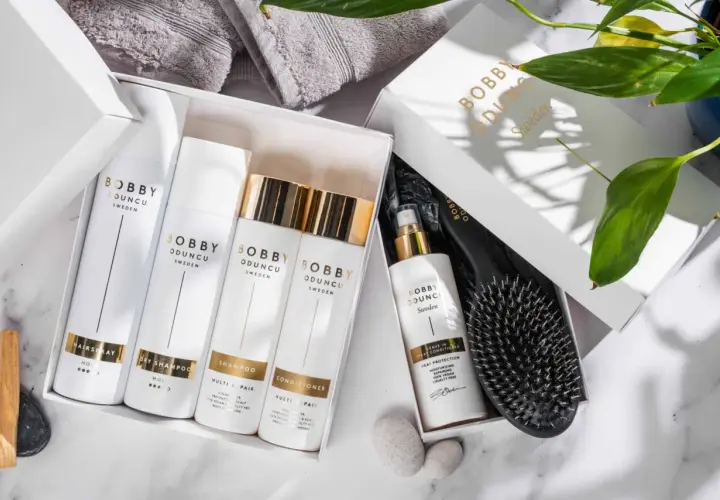 En presentbox med Bobby Oduncu-produkter för att ta hand om håret: hårspray, torrschampo, schampo, balsam och leave-in spray. En borste ligger bredvid.