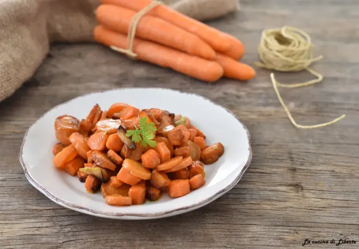 Carote in padella, dolci e caramellate, guarnite con prezzemolo fresco su un piatto bianco. Sullo sfondo, carote fresche legate con spago.