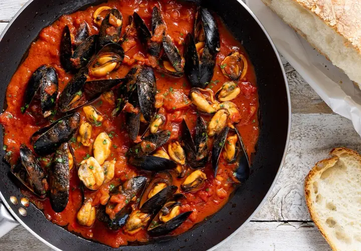 Cozze alla tarantina in padella, un piatto succulento con pane fresco a lato.