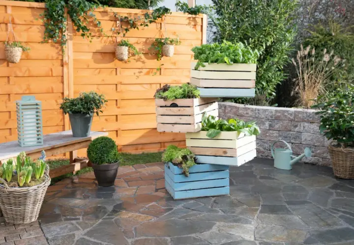 Fioriera fai da te con cassette di legno colorate, piene di verdure fresche, su un patio in pietra.