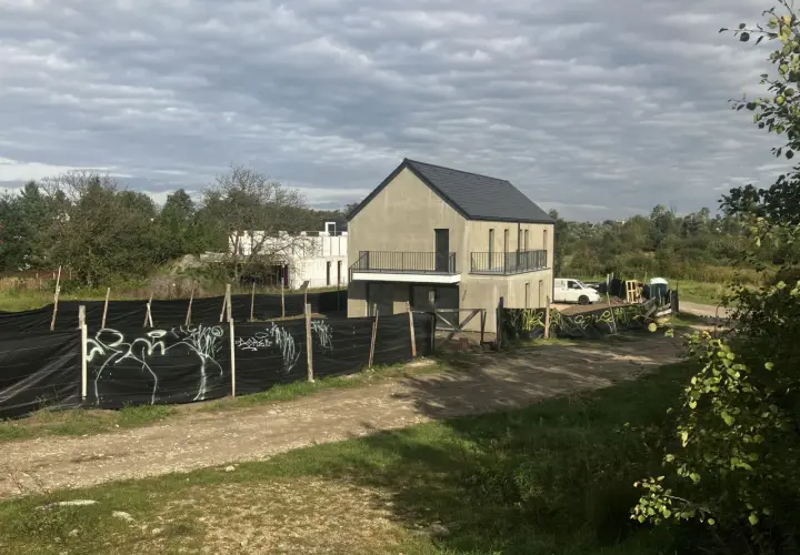 Plac budowy z niedokończonymi domami, ogrodzony czarną siatką z graffiti. Może to symbolizować zakaz budowy domów jednorodzinnych w tej okolicy.