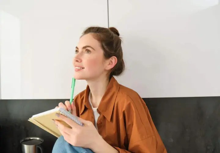 Ragazza pensosa, con un quaderno e una penna, dallo sguardo sognante. Una persona curiosa e operosa.