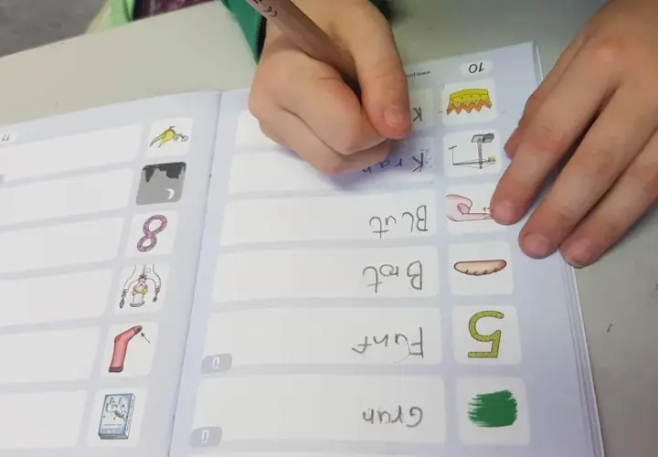 Kind schreibt im Rahmen des Förderunterrichts Grundschule Wörter wie "Kran" und "Brot" in ein Übungsheft.