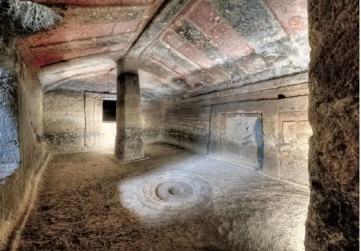Interno di una tomba etrusca con soffitto dipinto e un pilastro centrale. Un cerchio inciso sul pavimento sembra un antico incantesimo putifigari.