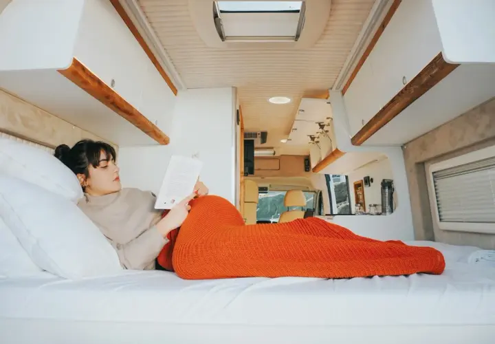 Une femme lit un livre, confortablement installée dans son camping-car fraîchement rénové. L'espace est lumineux et moderne.