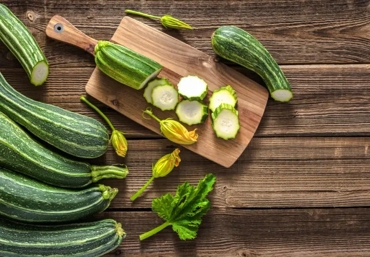 Frische Zucchini, einige roh geschnitten, liegen auf einem Holzbrett. Perfekt, um Zucchini roh zu essen!
