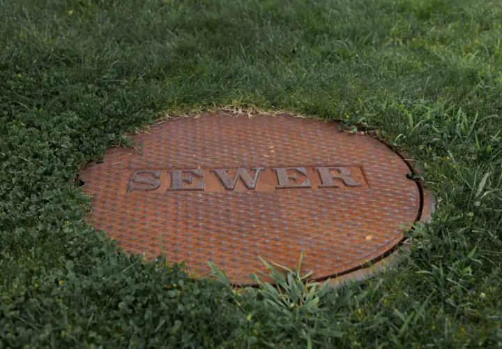 Zardzewiała pokrywa szamba z napisem "SEWER" w trawie. Czy na szambo trzeba mieć pozwolenie?