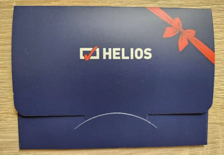 Chcesz wiedzieć, ile kosztuje voucher do kina Helios? Na zdjęciu widać elegancką, granatową kopertę z logo Helios i czerwoną wstążką, idealną na prezent.