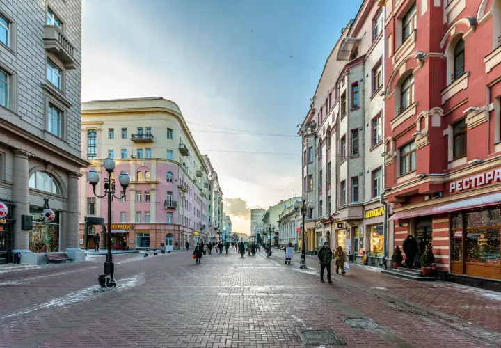 Zimowy spacer po Arbat w Moskwie. Ludzie przechadzają się brukowaną ulicą między kolorowymi kamienicami, a w oknach sklepów migoczą świąteczne dekoracje.