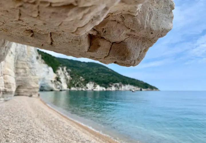 Vue depuis une grotte sur une plage de galets, mer turquoise et falaises blanches sur la côte adriatique Italie.