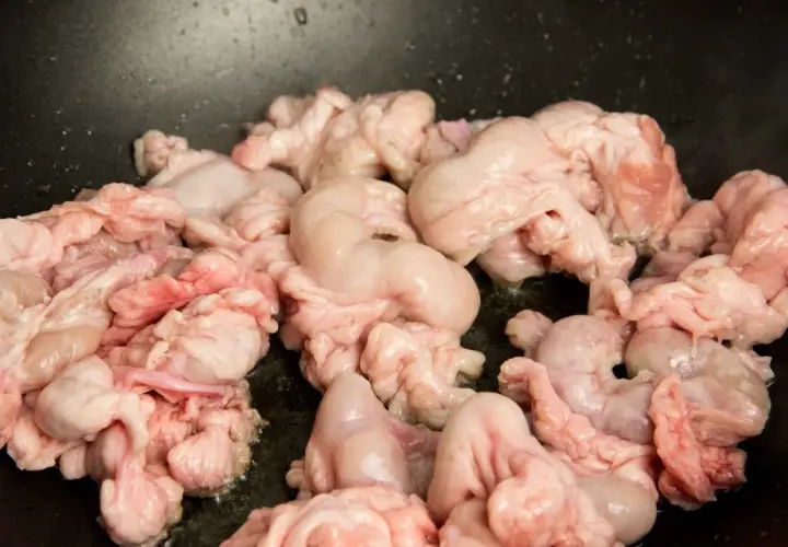 Unos gallinejas y entresijos crudos se cocinan en una sartén negra, listos para ser un plato tradicional.