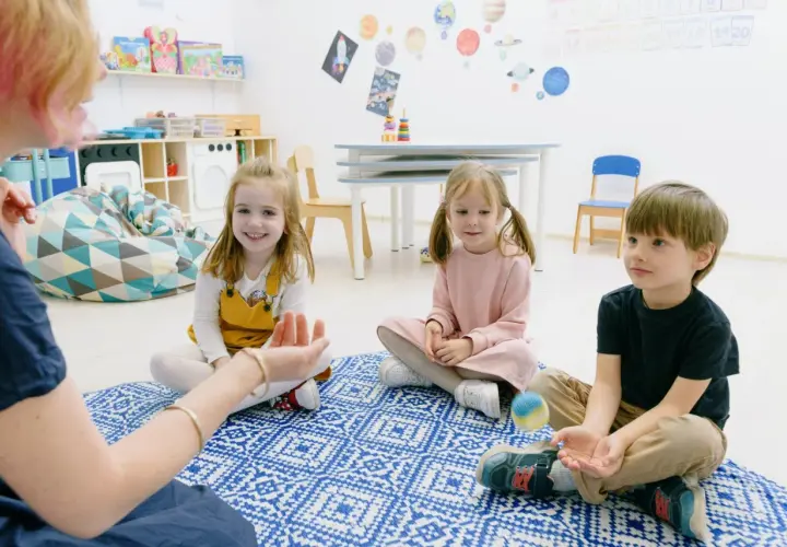 Dzieci biorą udział w zabawach integracyjnych w przedszkolu, siedząc na dywanie i słuchając nauczycielki.