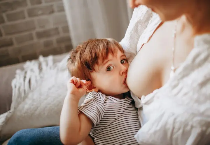 Un bimbo con occhi grandi e curiosi viene allattato dalla mamma. Un momento intimo, un gesto naturale, un esempio di allattare in pubblico senza timori.