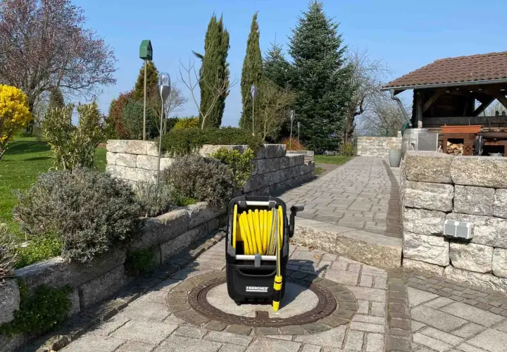 Ein gelber Schlauchwagen steht auf einem gepflasterten Weg im Garten, bereit für die Gartenarbeit.