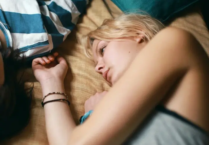 Två unga kvinnor ligger nära varandra, en med blont hår och en med mörkt. En scen som påminner om svenska ungdomsfilmer från 90-talet.