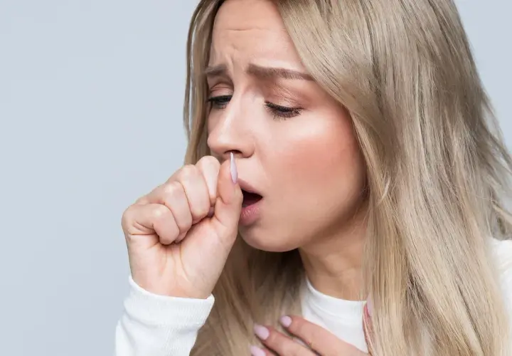 Mujer rubia con expresión de malestar, tosiendo y sujetándose el pecho. Sufre dolor en el pecho al toser sin fiebre.
