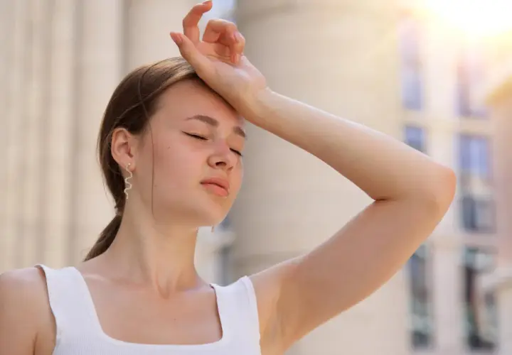 Une jeune femme essuie sa sueur sous un soleil de plomb, se demandant combien de temps dure un coup de chaleur.