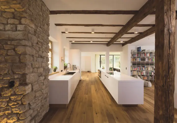 Modernes Wohnen mit Fachwerk: Eine Küche mit weißen Inseln und Holzbalken, die das Fachwerk innen gestalten.