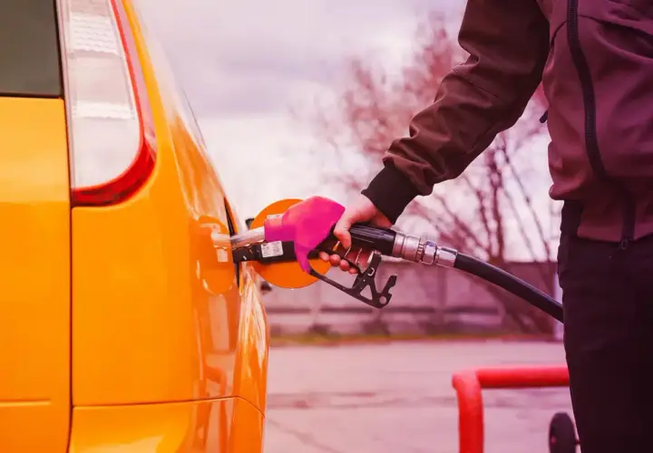 Mano con guanto rosa inserisce la pompa di benzina nel serbatoio di un'auto arancione. Il **consumo auto** è una spesa da considerare.