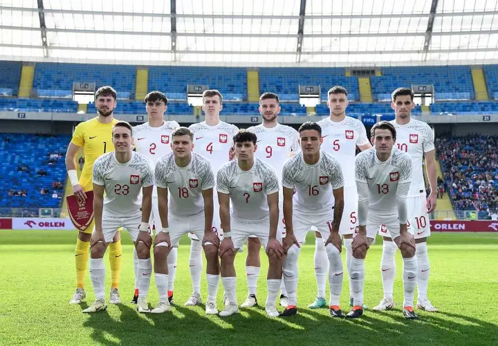 Młodzieżowa reprezentacja Polski w piłce nożnej pozuje do zdjęcia na stadionie.