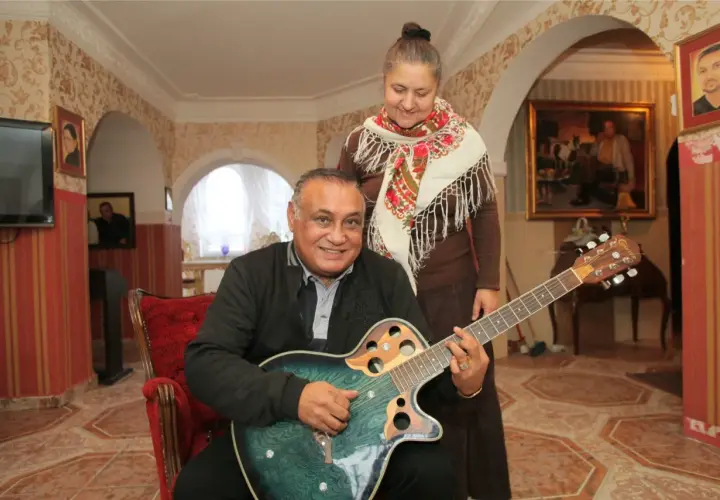 Uśmiechnięty mężczyzna gra na gitarze, a za nim stoi kobieta. Nie wiadomo, ile lat ma Don Vasyl, ale wygląda na szczęśliwego.
