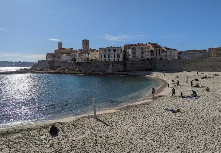 Sonniger nizza strand mit Menschen, die sich entspannen, und einer historischen Stadt im Hintergrund.