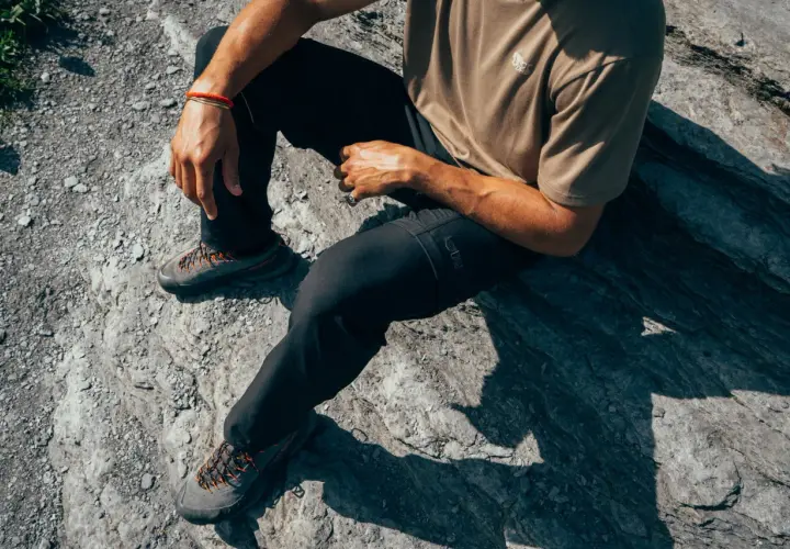 Man sitting on rocks, wearing black pants and hiking shoes. The shoes are grey with orange laces, perfect for schoenen oprekken on any terrain.