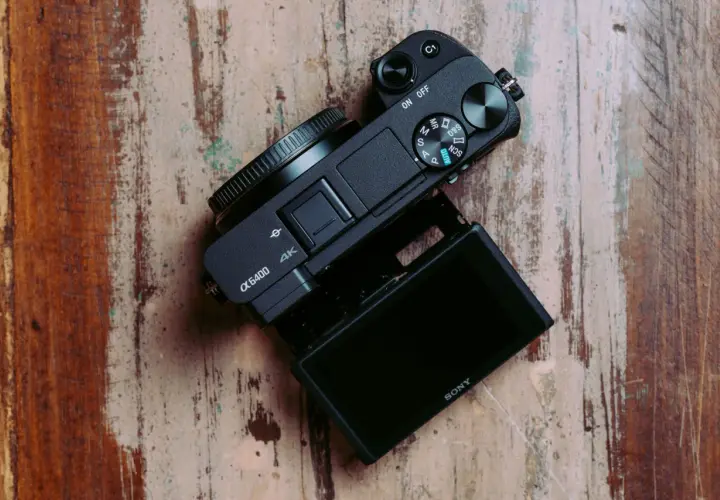 Czarny aparat Sony α6400 z uchylnym ekranem leży na drewnianym blacie. Idealny do testów i vlogowania.