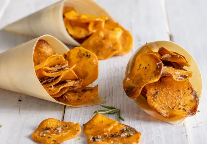 Croccanti patate dolci in padella, condite con erbe aromatiche e sale, servite in coni di legno.