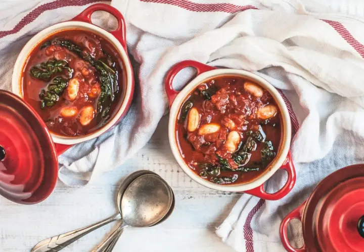 Due ciotole rosse con zuppa di cavolo nero e fagioli, pronte per essere gustate.